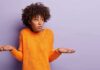 person shrugging in orange sweater against purple background