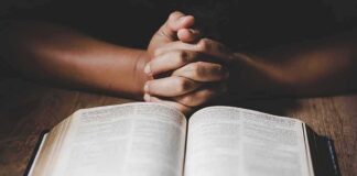 Hands clasped over an open book on a wooden table