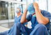 Two exhausted healthcare workers in scrubs sit on the floor