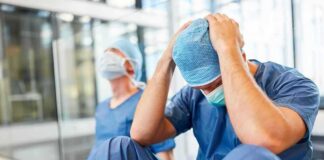 Two exhausted healthcare workers in scrubs sit on the floor
