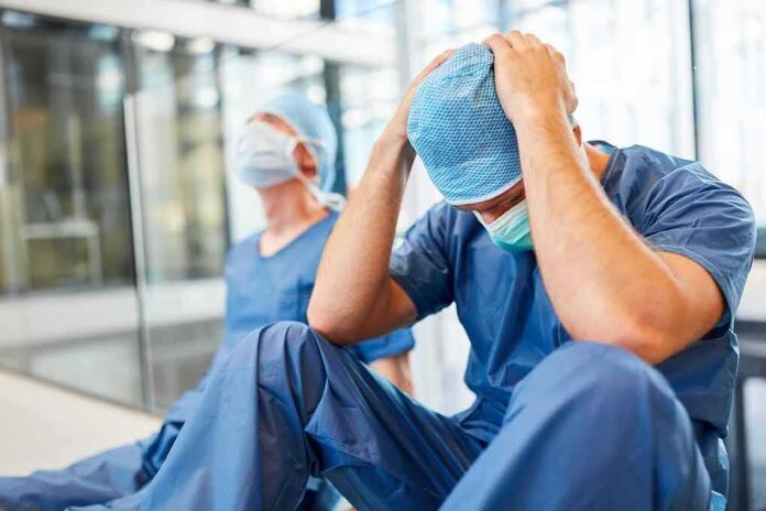 Two exhausted healthcare workers in scrubs sit on the floor