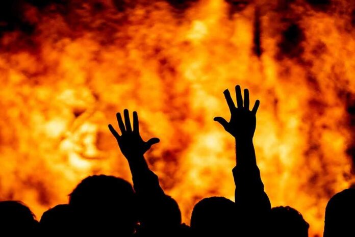 silhouetted hands raised before a large fire