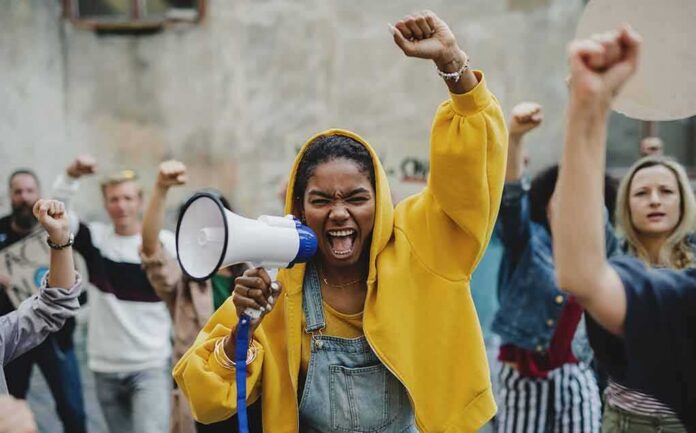 shutterstock_1841074540 Protester in yellow hoodie shouting into a megaphone