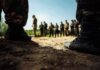 Status Pass? Uneven Justice Alleged In Olive Field Soldiers in boots framing a group standing in a field