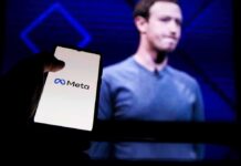 Wealth Tax Panic Freezes Zuckerberg In Place Mark Zuckerberg on screen with a hand holding a phone showing the Meta logo