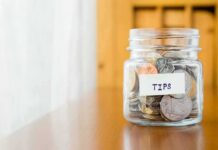 Tip jar filled with assorted coins on a wooden counter