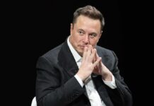 Musk Joins Pentagon’s New War Brain Elon Musk seated in a dark setting with hands steepled near his face
