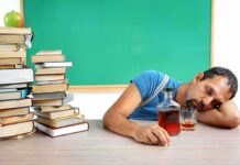 Man sleeping at a desk with a glass and bottle of liquor