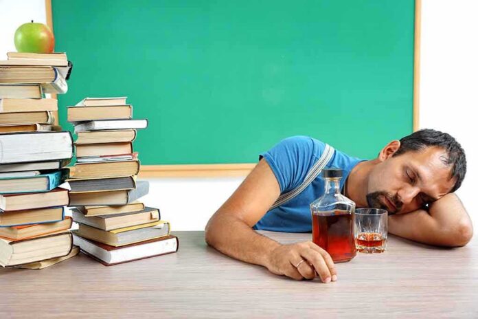 shutterstock_419468695 Man sleeping at a desk with a glass and bottle of liquor