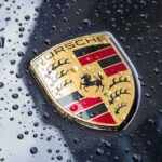 Luxury Squeeze: Porsche Cuts, Charges More Porsche crest on wet car hood