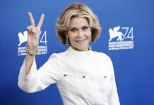 Jane Fonda posing with a peace sign against a blue backdrop